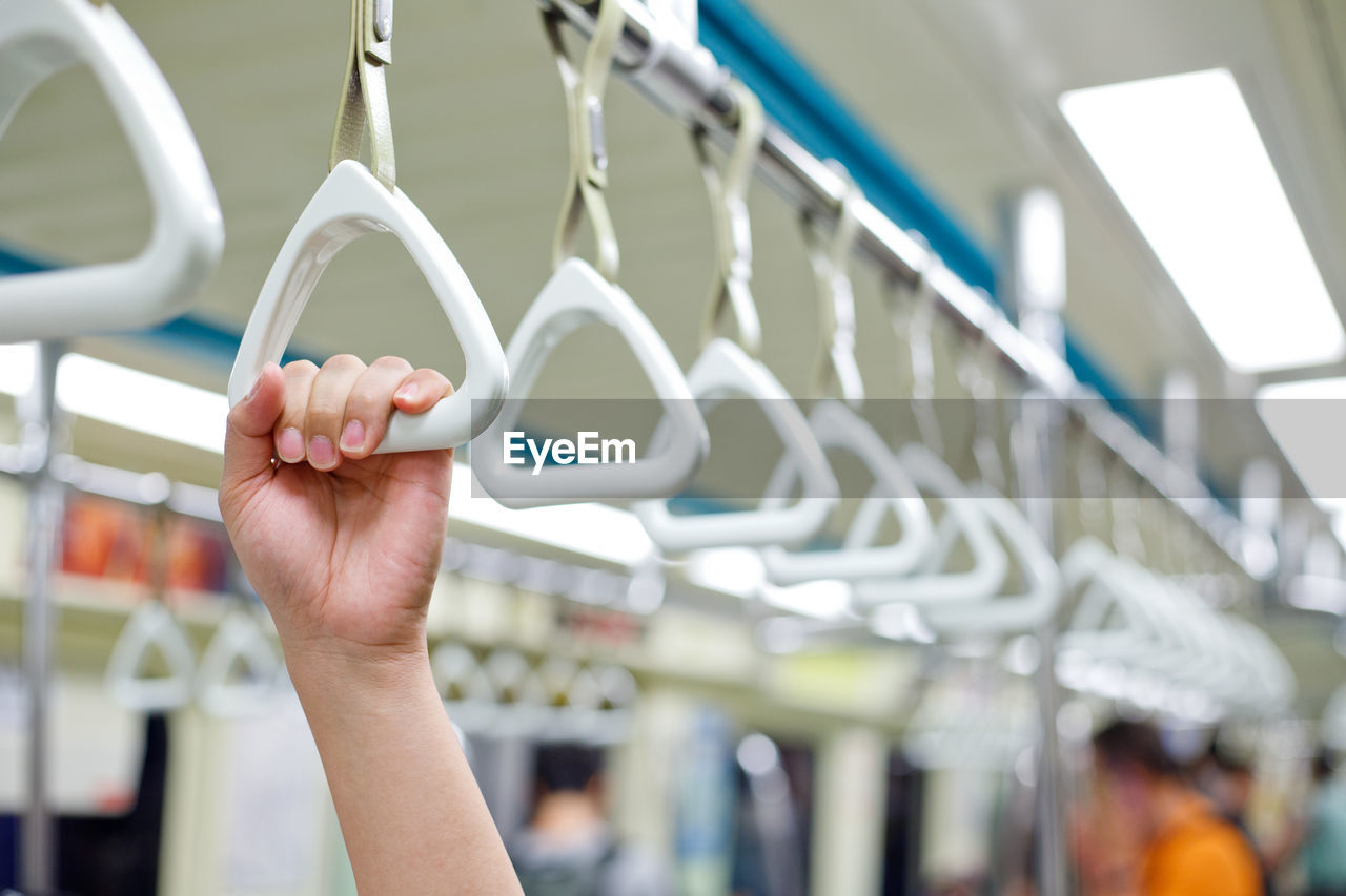 Cropped hand of person holding handle hanging in train