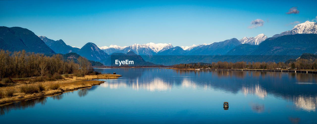 Panoramic view of lake by mountains against blue sky