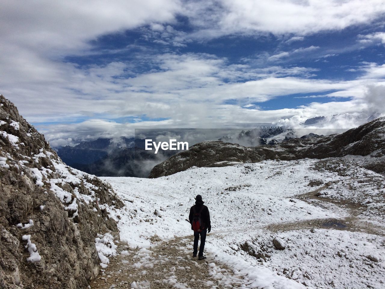 Rear view of man standing on snowcapped mountain against sky