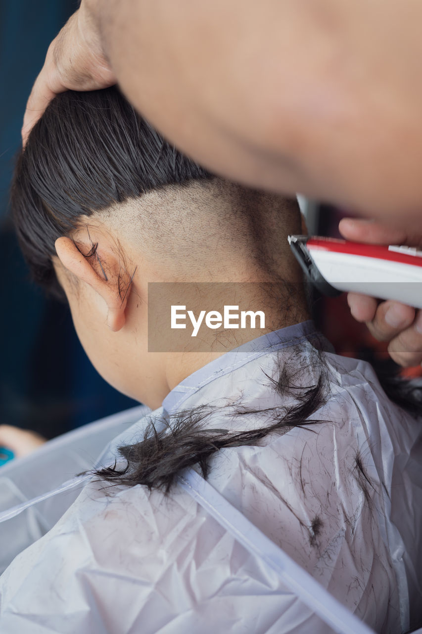 A young boy is getting haircut at home from the father using electronic shaver. view from side.