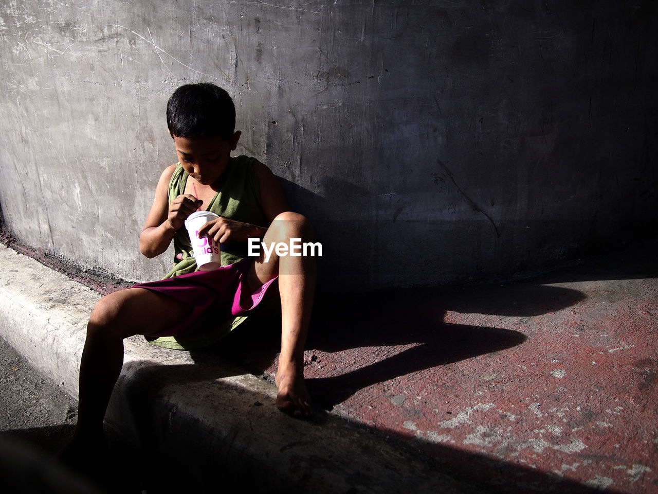 REAR VIEW OF BOY SITTING ON WALL