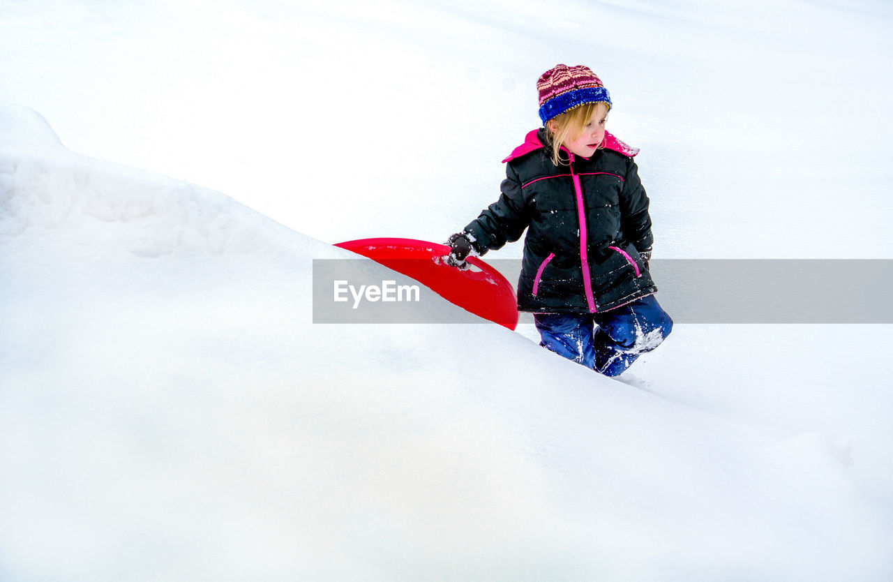 Adorable little girl walks through the snow with her red sled