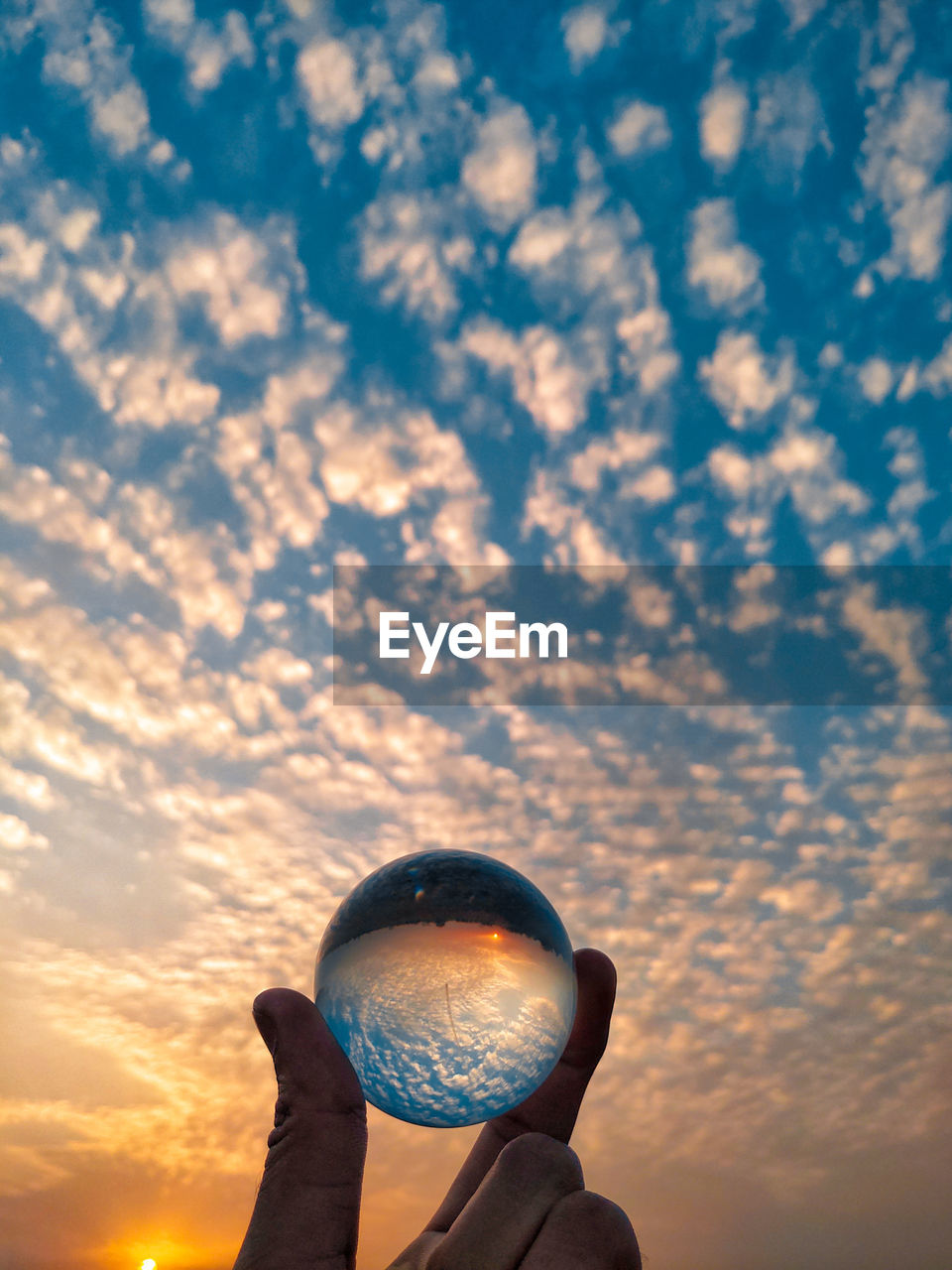 LOW ANGLE VIEW OF HAND HOLDING ORANGE AGAINST SKY