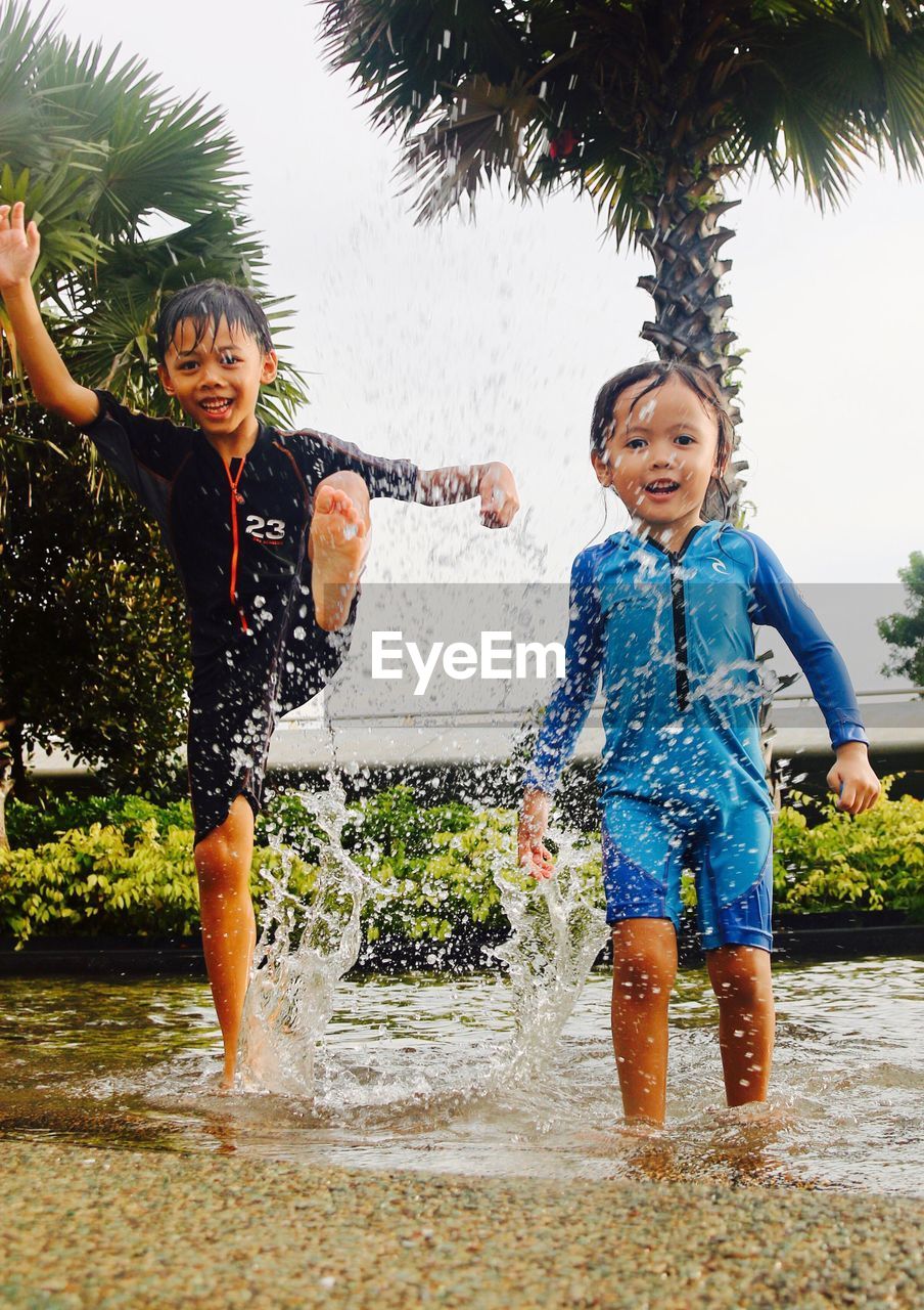 Portrait of siblings playing in pond against sky