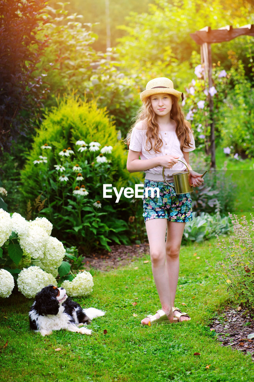 Portrait of smiling girl standing with watering can by plants and dog