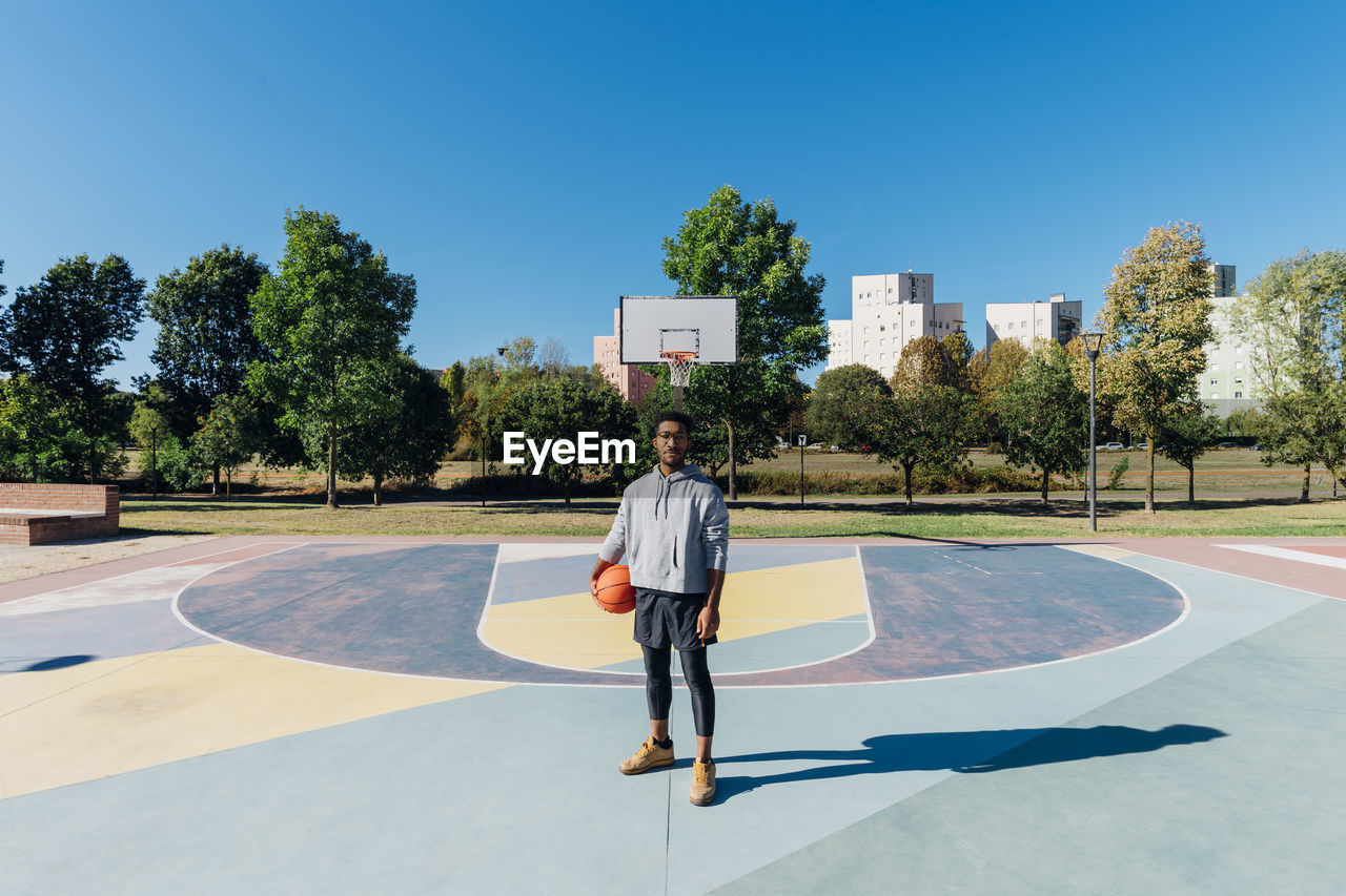 Young sportsman with basketball in sports court on sunny day