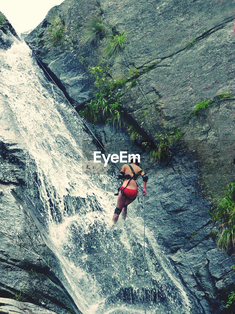 Low angle view of woman in bikini climbing rock formation