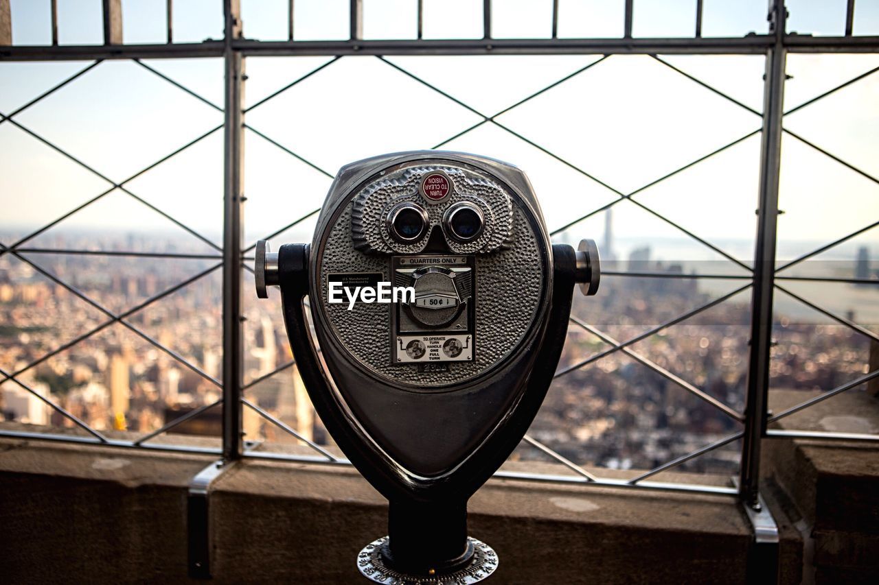 Coin-operated binoculars by cityscape against sky