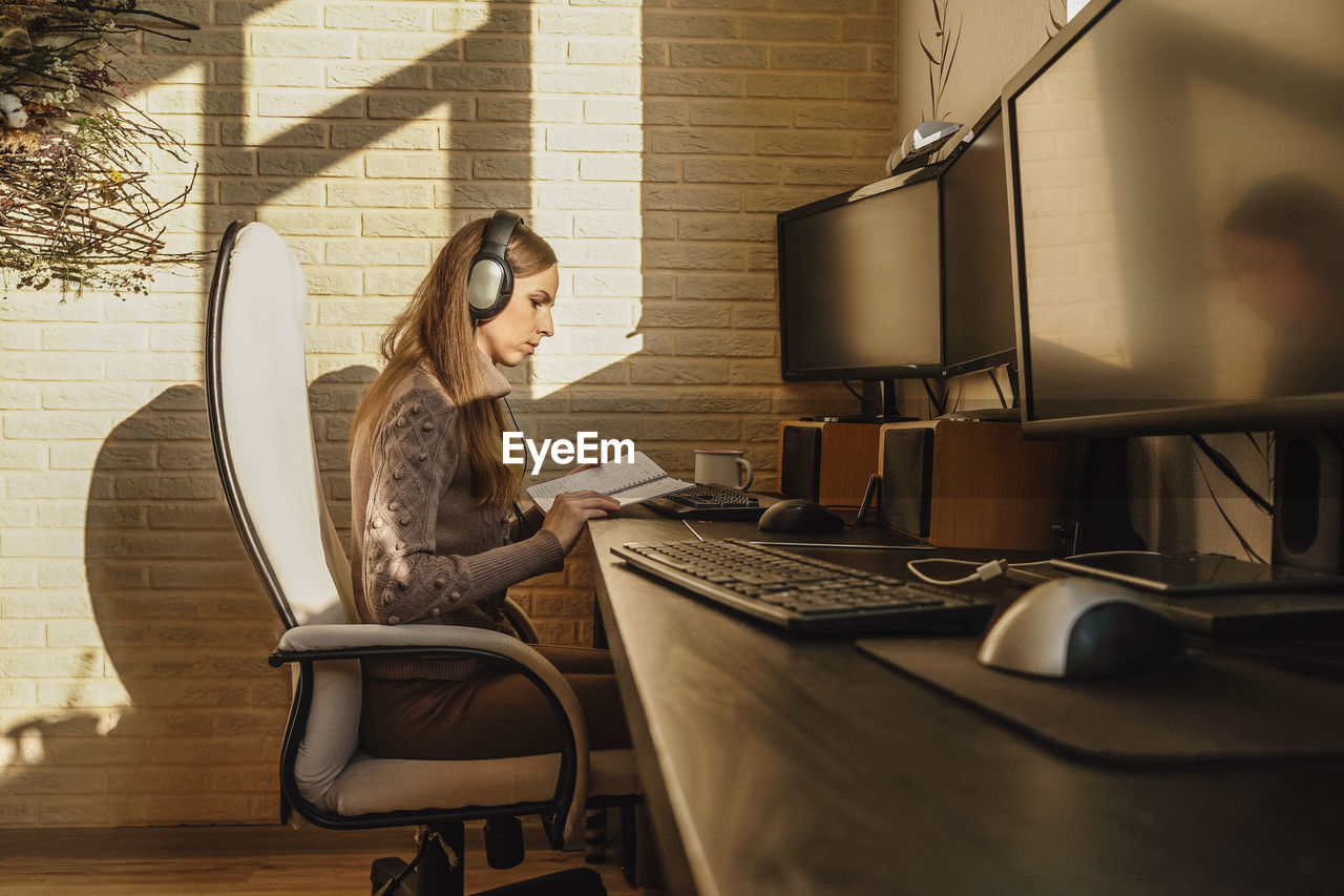 Woman reading book by computer on table