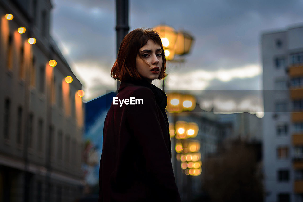 Portrait of young woman standing in illuminated city