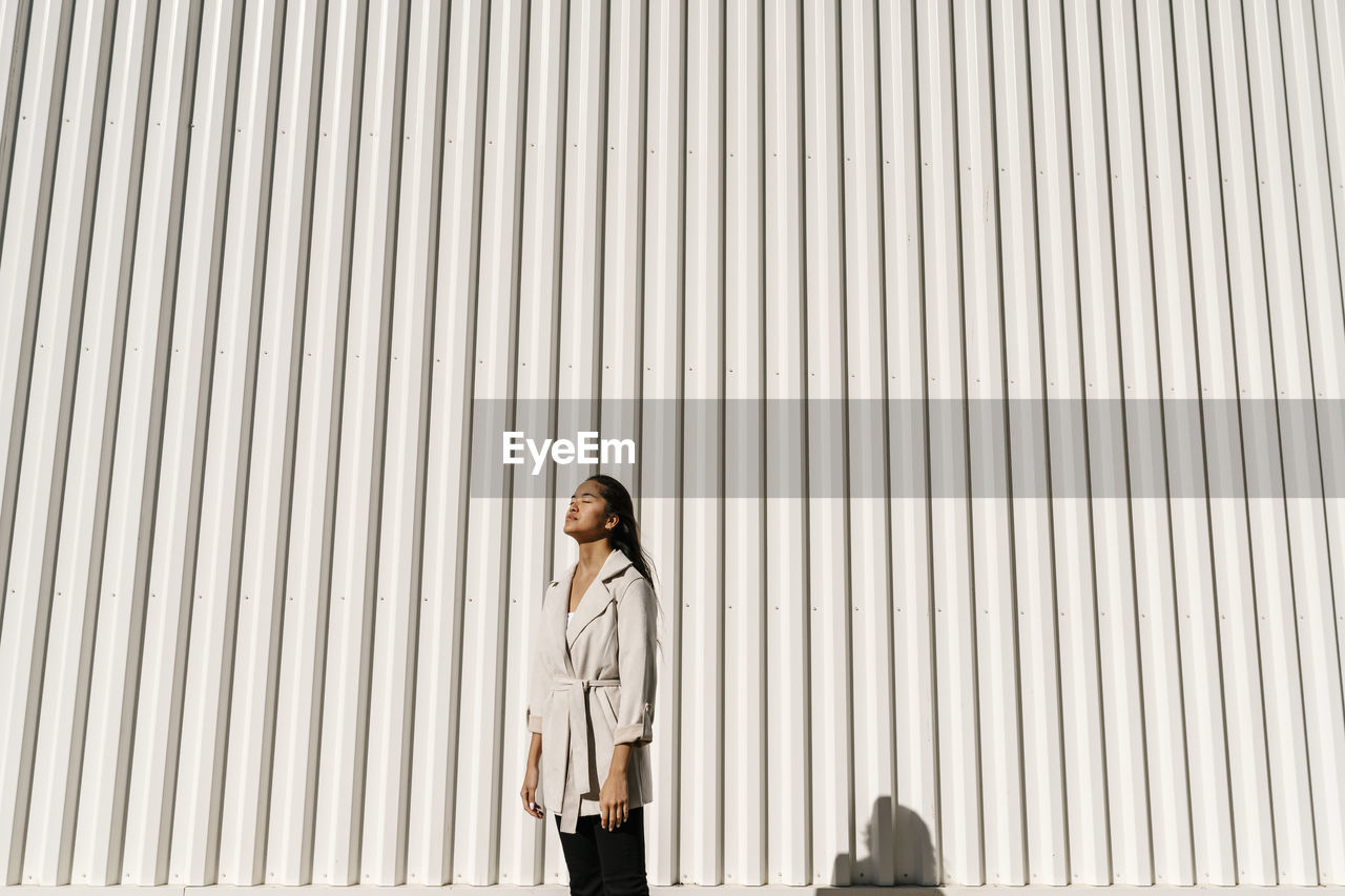 Young elegant woman with eyes closed in front of white wall