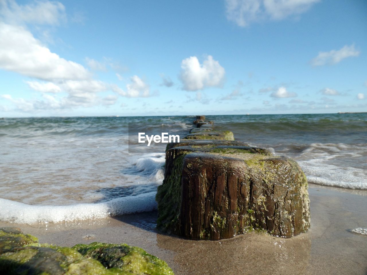 Wooden posts in sea against sky