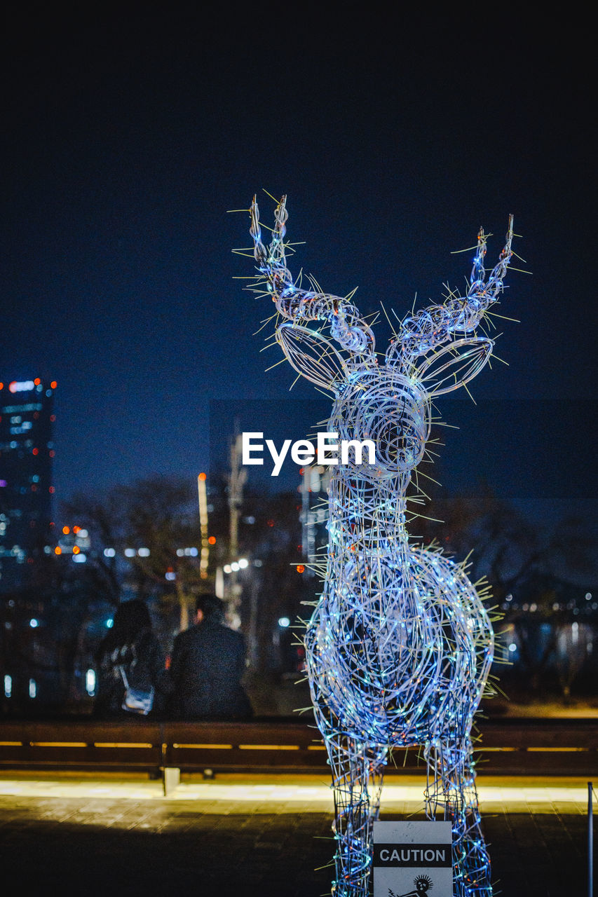 CLOSE-UP OF ILLUMINATED SCULPTURE AGAINST BUILDING