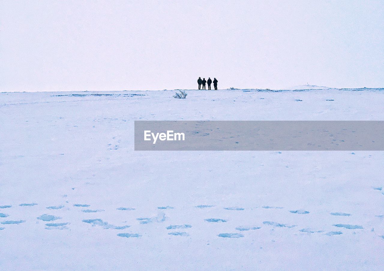 People standing on snow covered landscape against clear sky