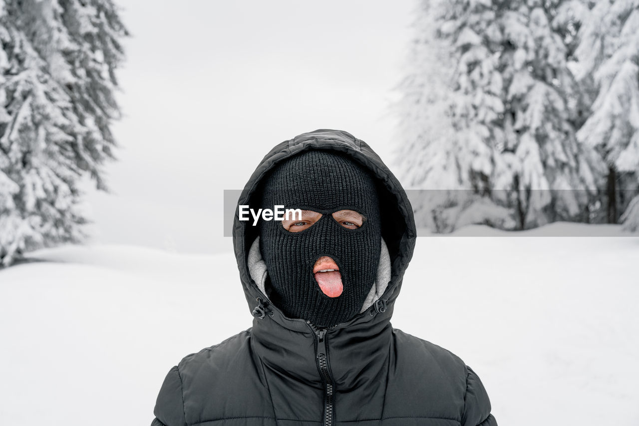 Man with ski mask sticking out tongue in winter forest