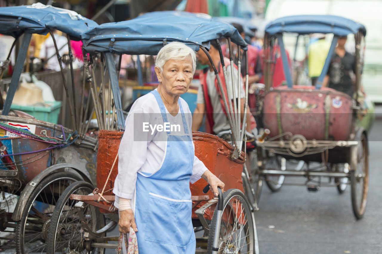 Senior woman standing by jinrikishas on road