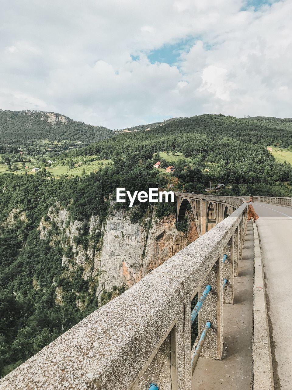 Woman standing by railing against cloudy sky