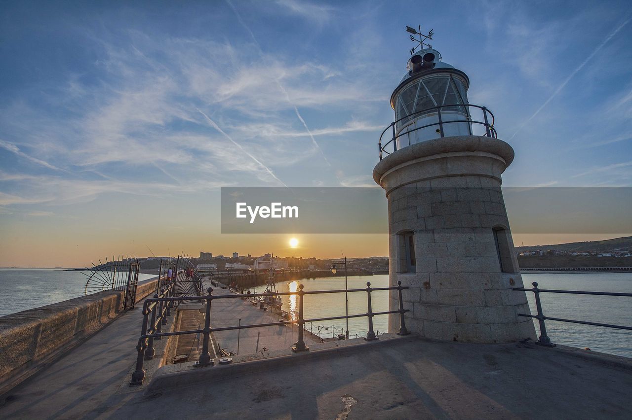 Lighthouse by sea against sky during sunset