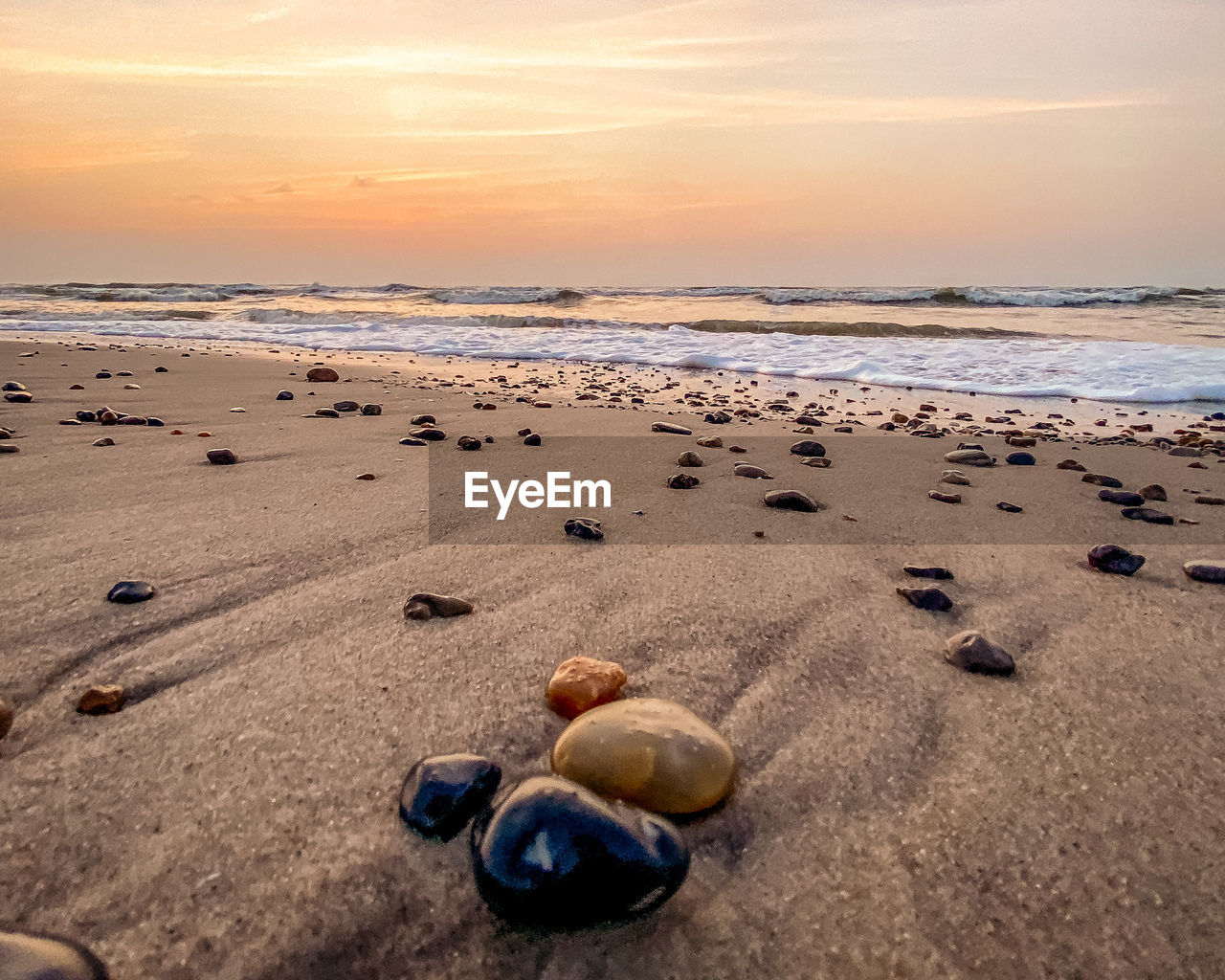 Surface level of pebbles on beach against sky during sunset