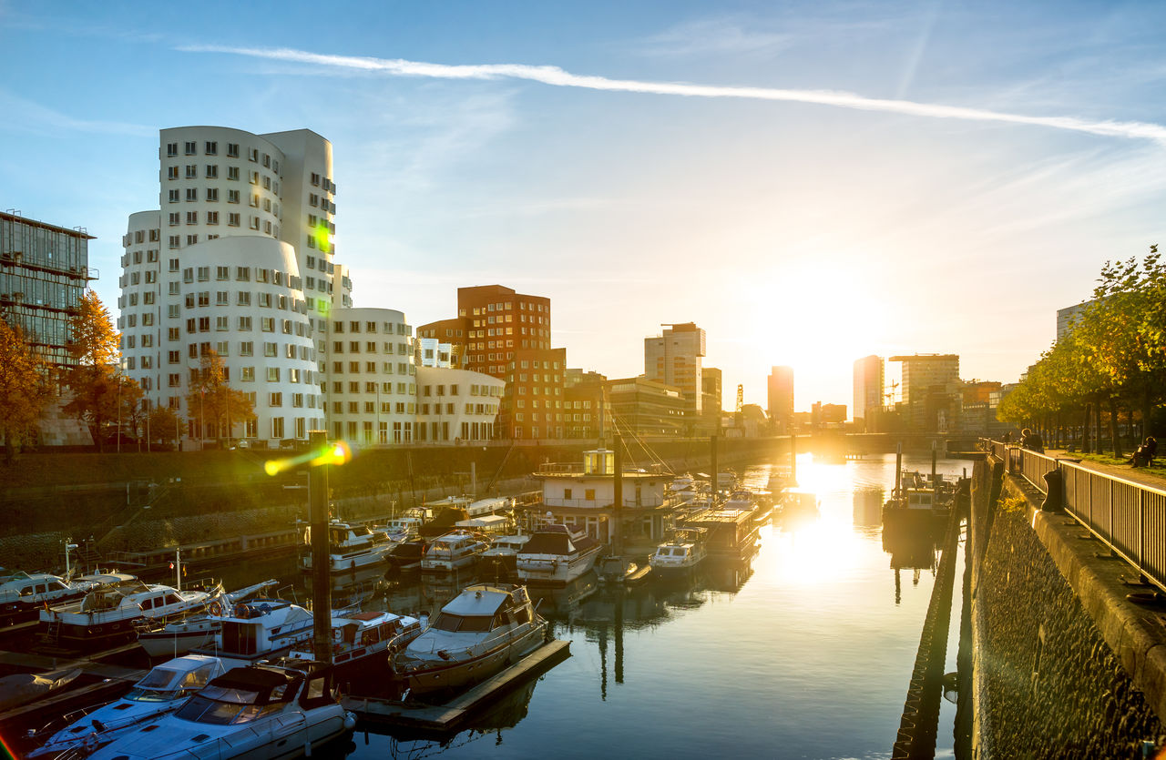 Boats moored in city against sky during sunset