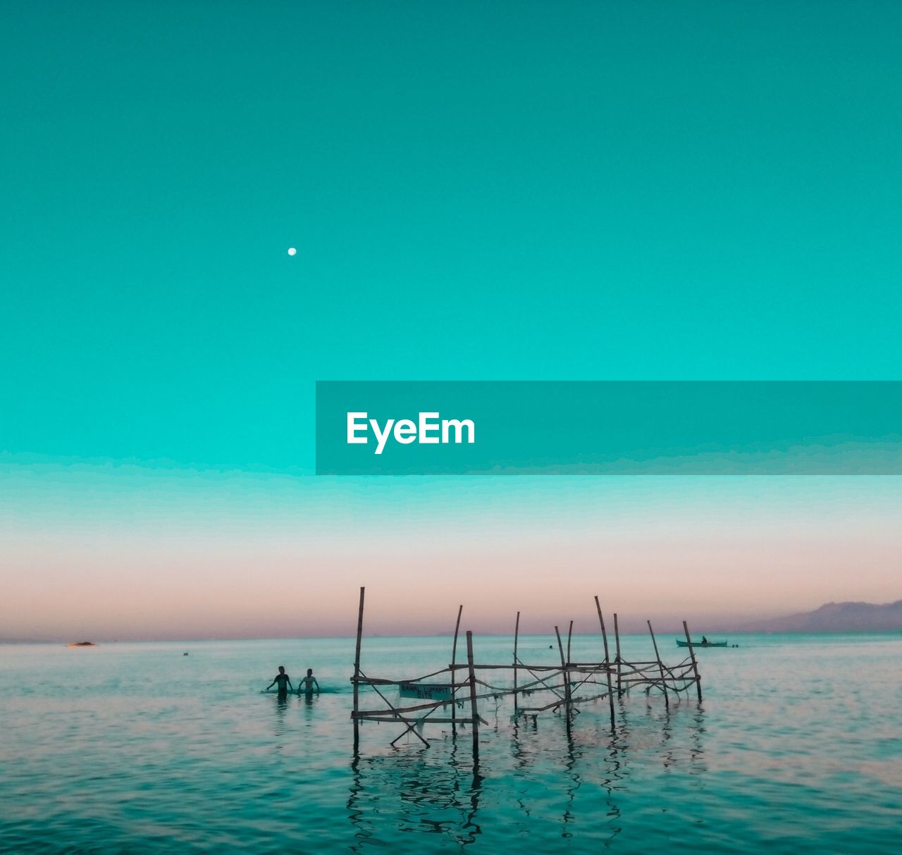 People in sea against clear sky during sunset