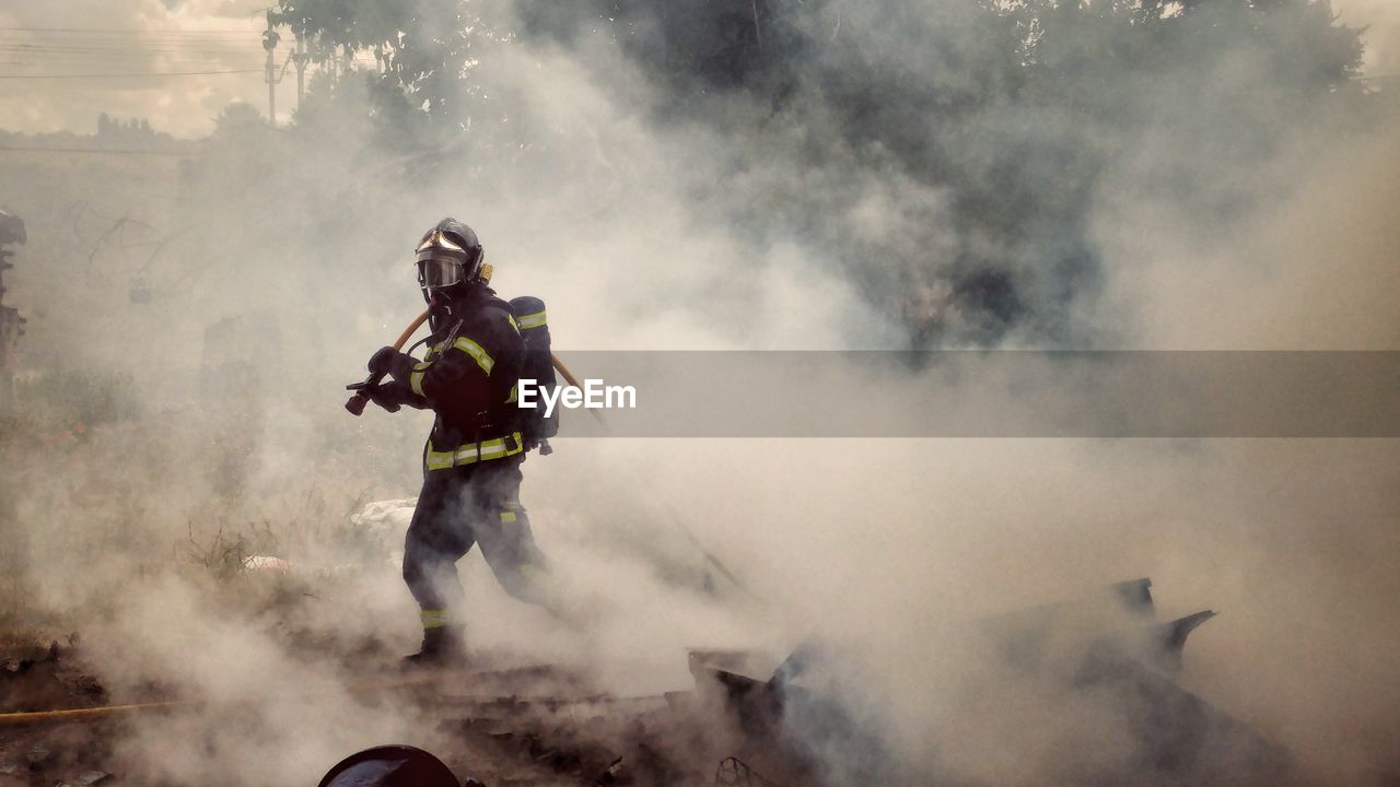 Full length of firefighter walking amidst smoke