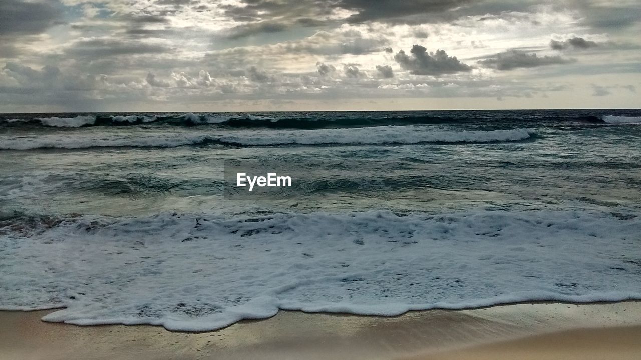 View of calm beach against cloudy sky