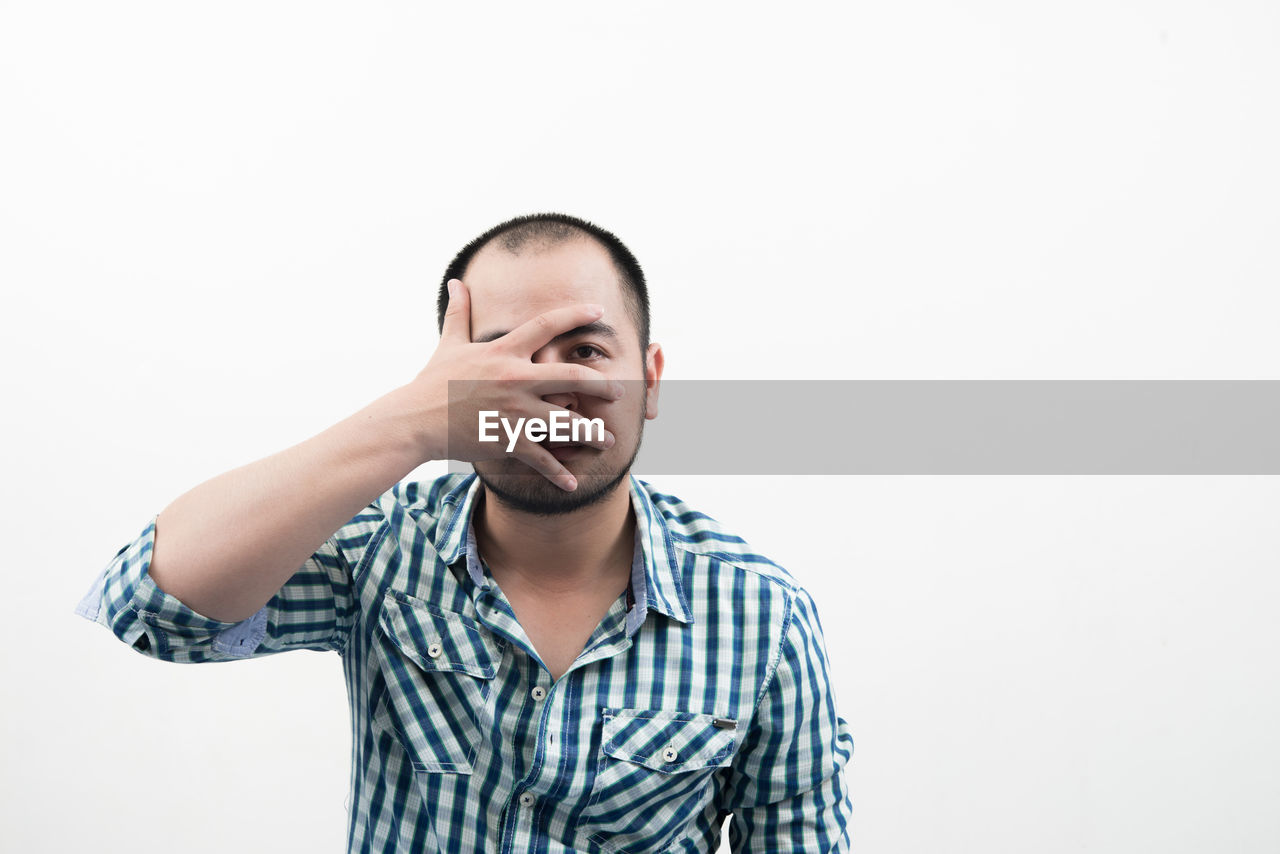 Portrait of mid adult man covering face against white background