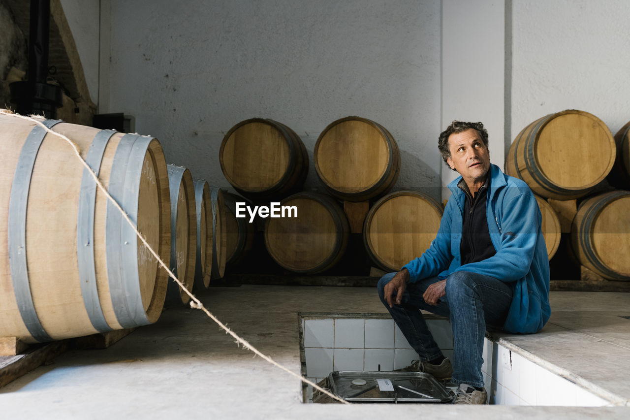 Mature male worker sitting amidst barrels at winery