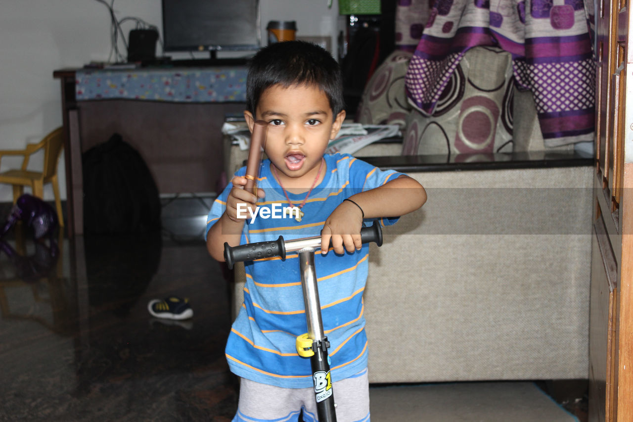 Portrait of cute boy standing on push scooter at home