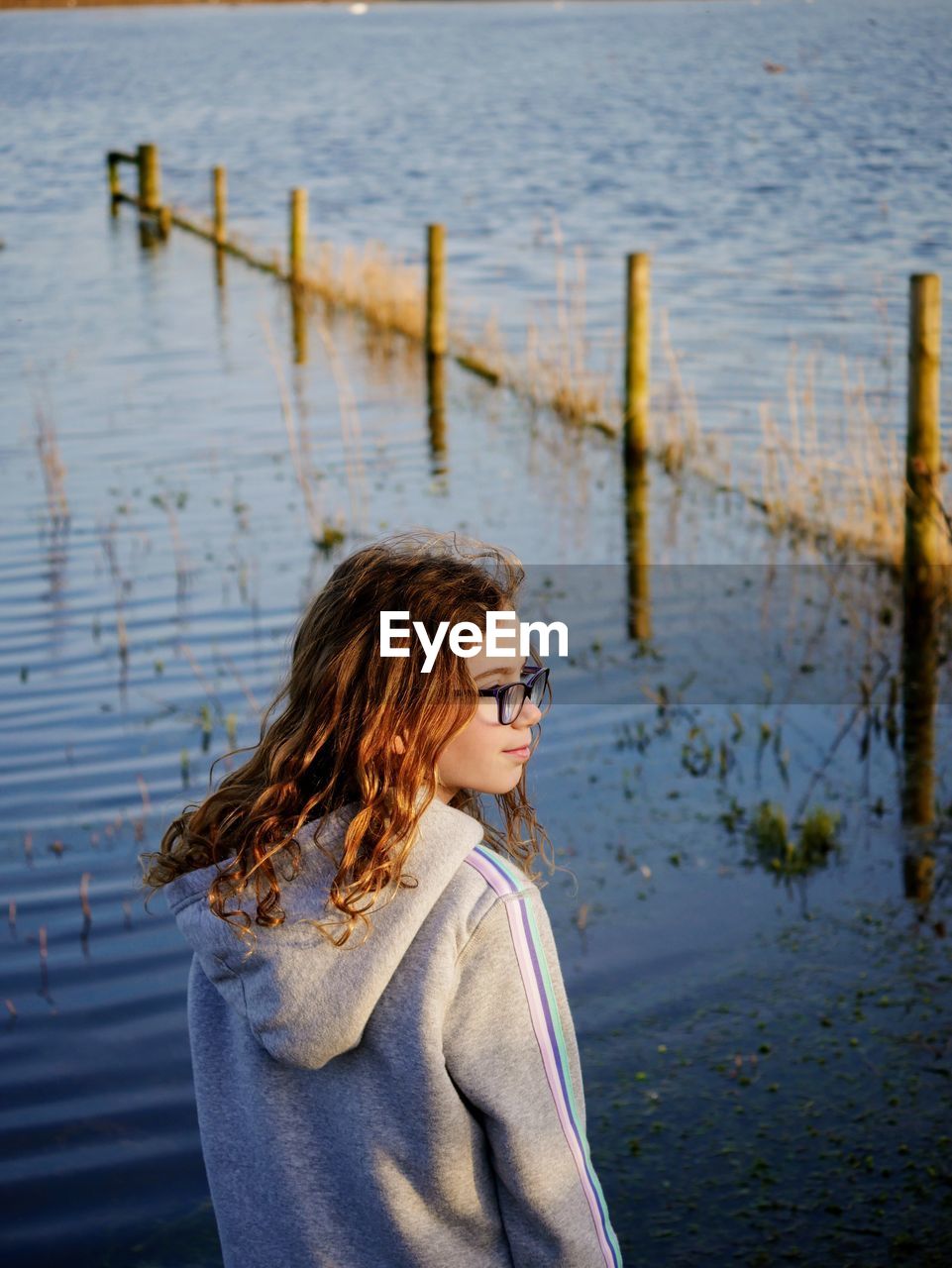 Girl looking away while standing by lake