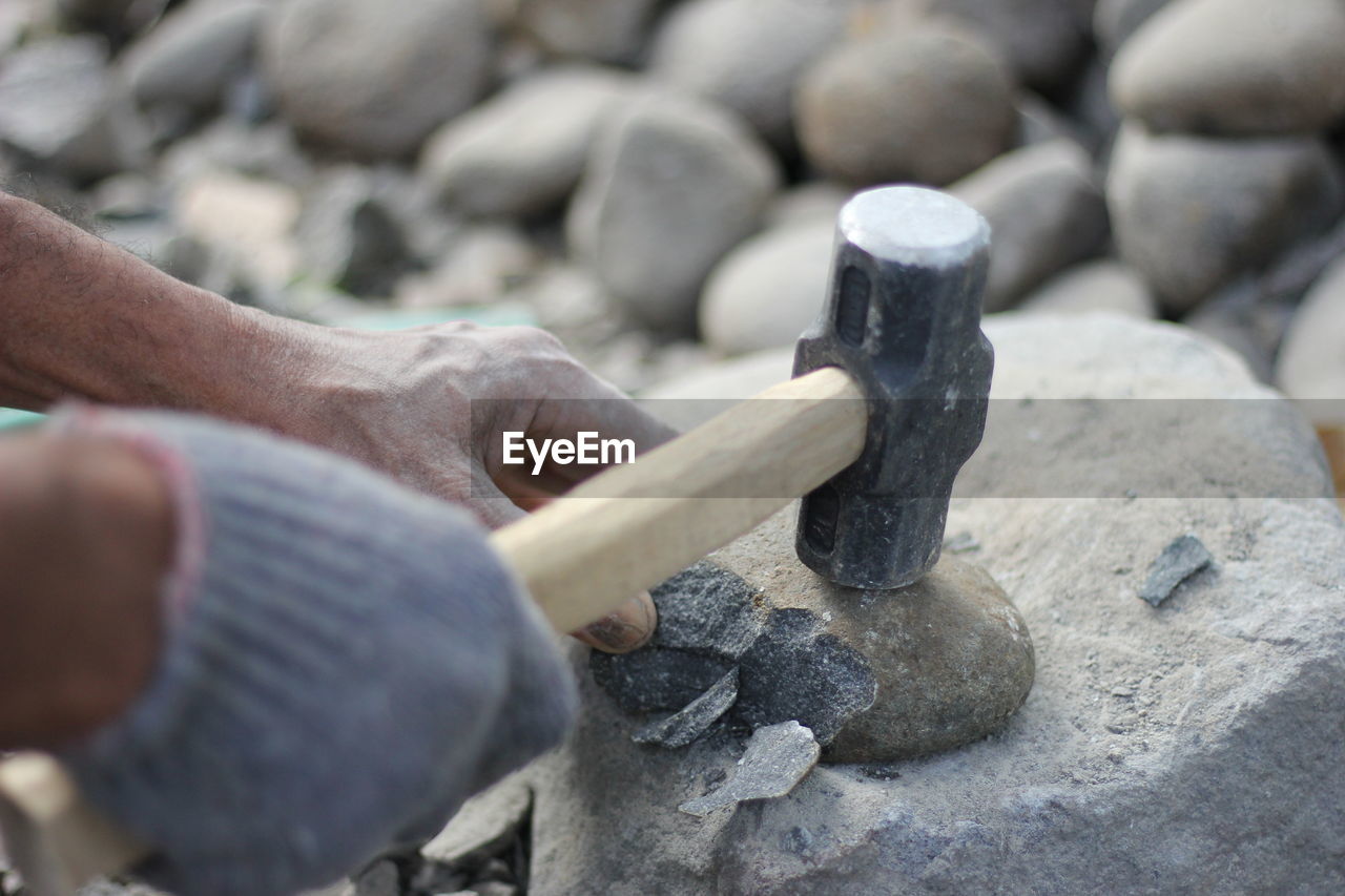 Cropped hands breaking stone with hammer