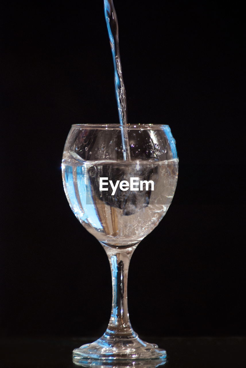 Close-up of water glass on glass against black background