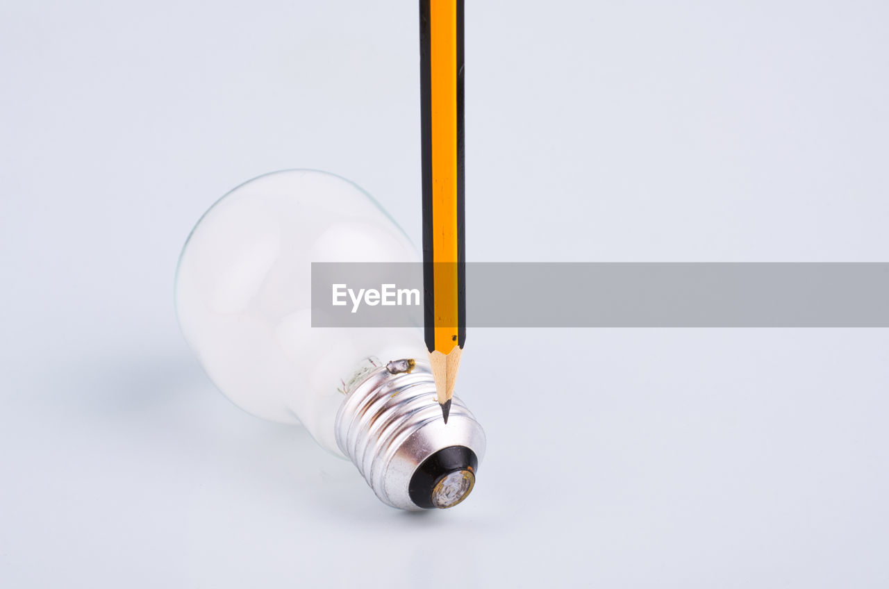 Close-up of pencil over light bulb against white background