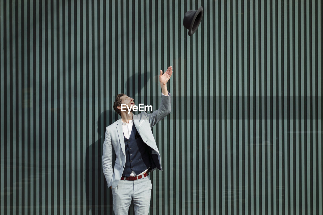 Businessman throwing hat while standing against wall