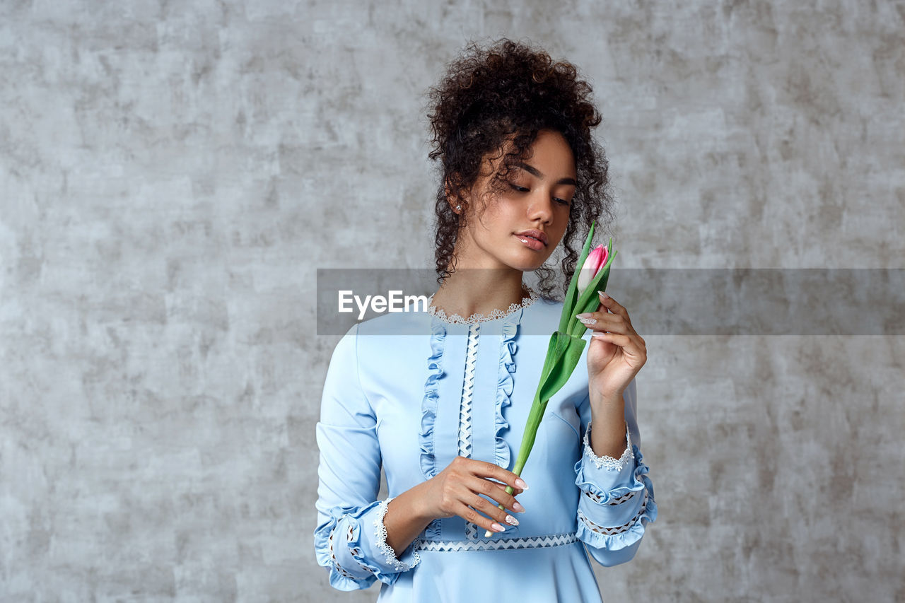 Beautiful woman holding tulip while standing against wall