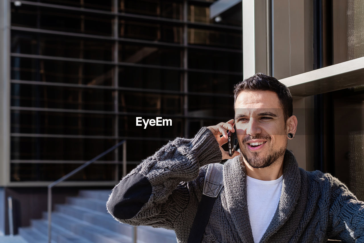 Man using smartphone outdoors, standing next to office building