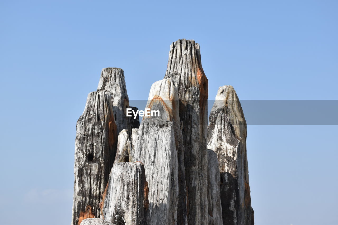 High section of wooden post against clear sky on sunny day