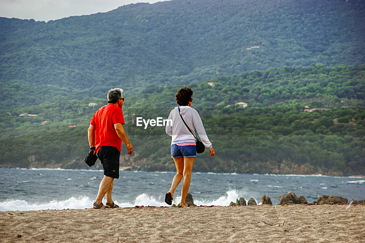 REAR VIEW OF MEN STANDING ON BEACH