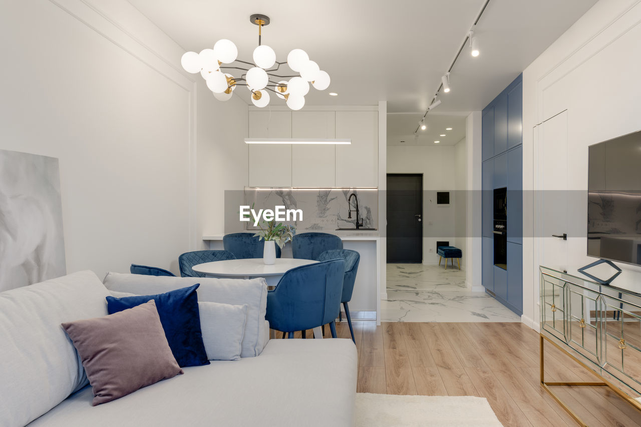 Bright living room with dining table and mirror table, blue chairs and curtains