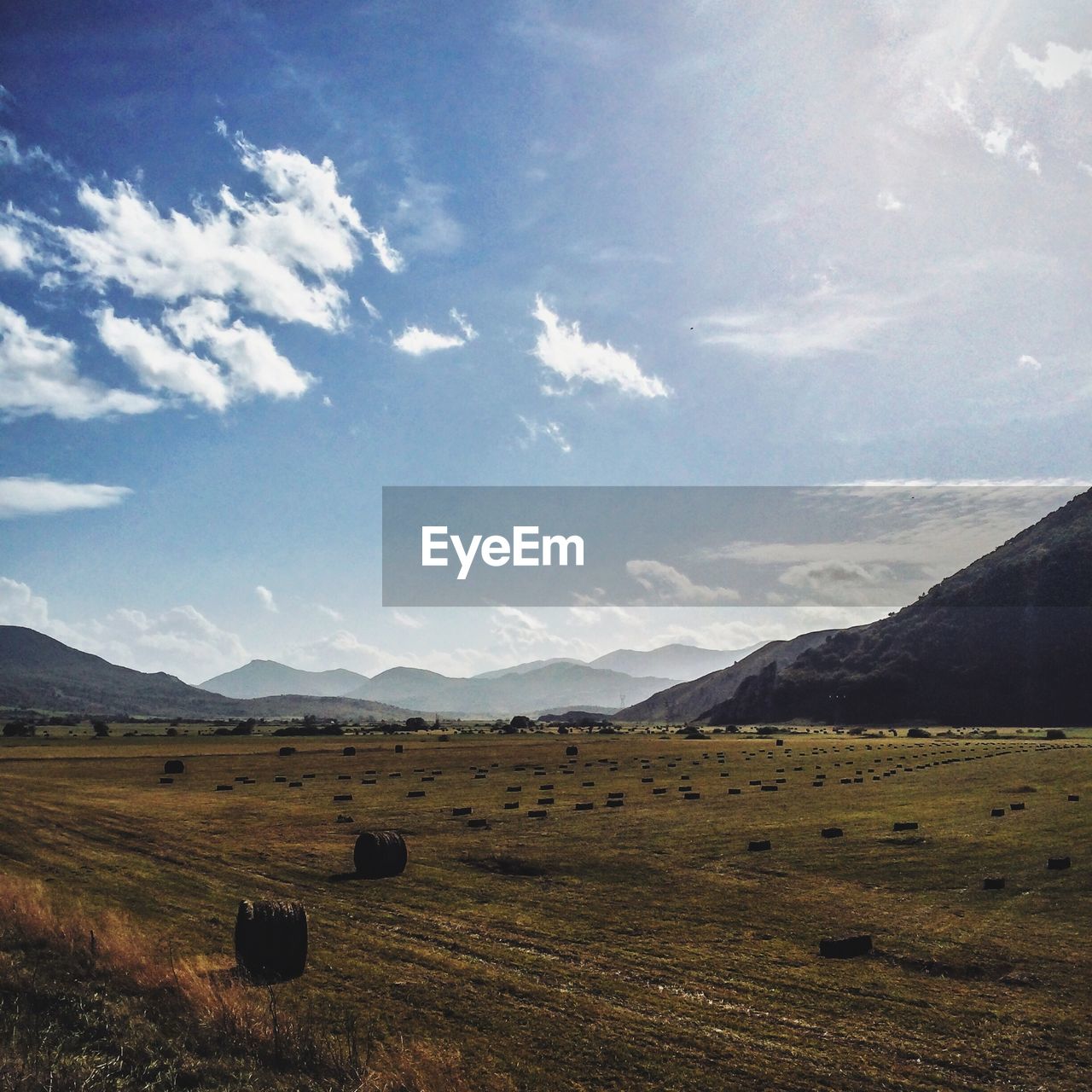 Hay bales on field against cloudy sky