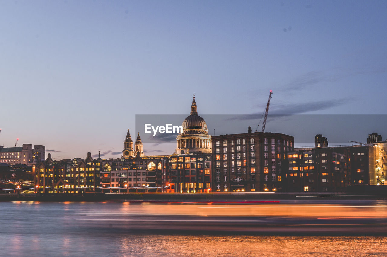 Light trails in river against historic church in illuminated city at dusk