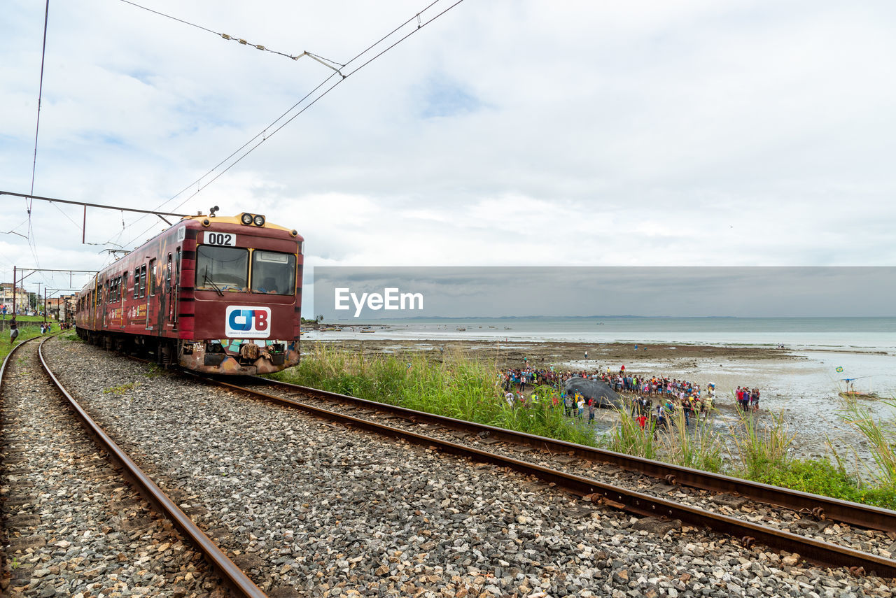 railroad track, track, transportation, rail transportation, mode of transportation, sky, cloud, train, public transportation, railway, vehicle, nature, travel, transport, water, locomotive, day, sea, motion, land vehicle, outdoors, group of people, land, freight transportation, on the move, electricity, journey