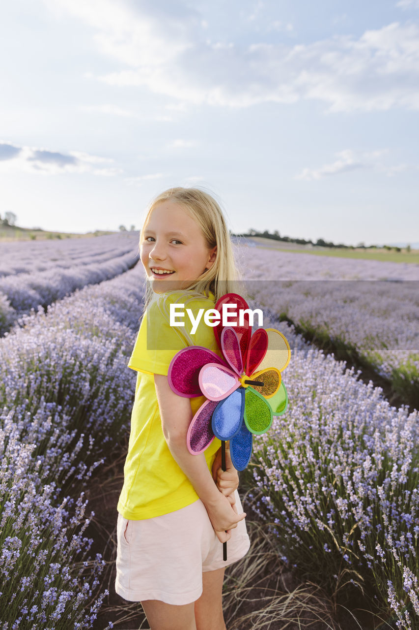Smiling blond girl holding pinwheel toy in lavender field