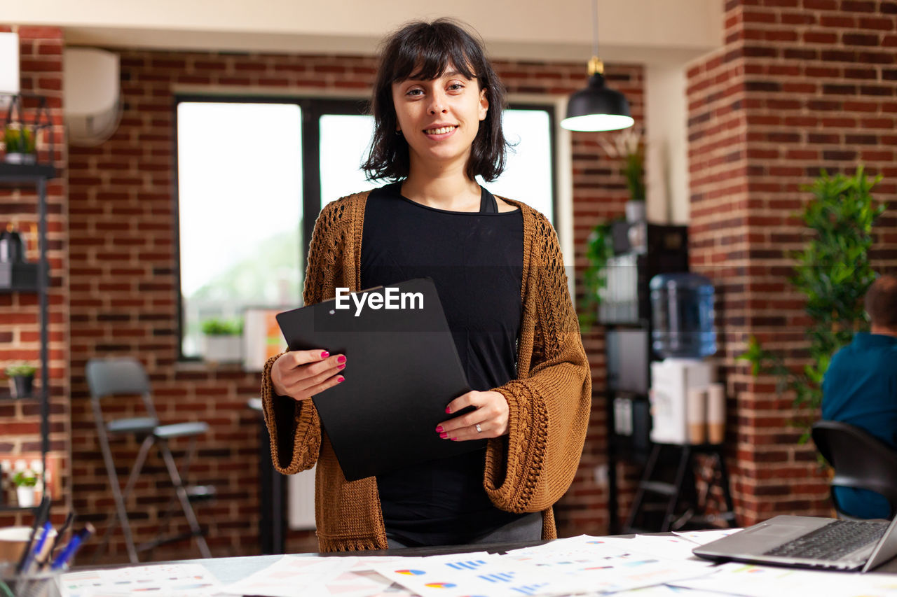 portrait of smiling young woman using digital tablet while standing in office
