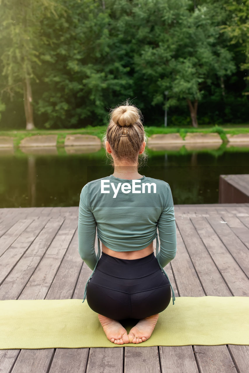 A some woman sitting , on a wooden platform by a pond in the park.