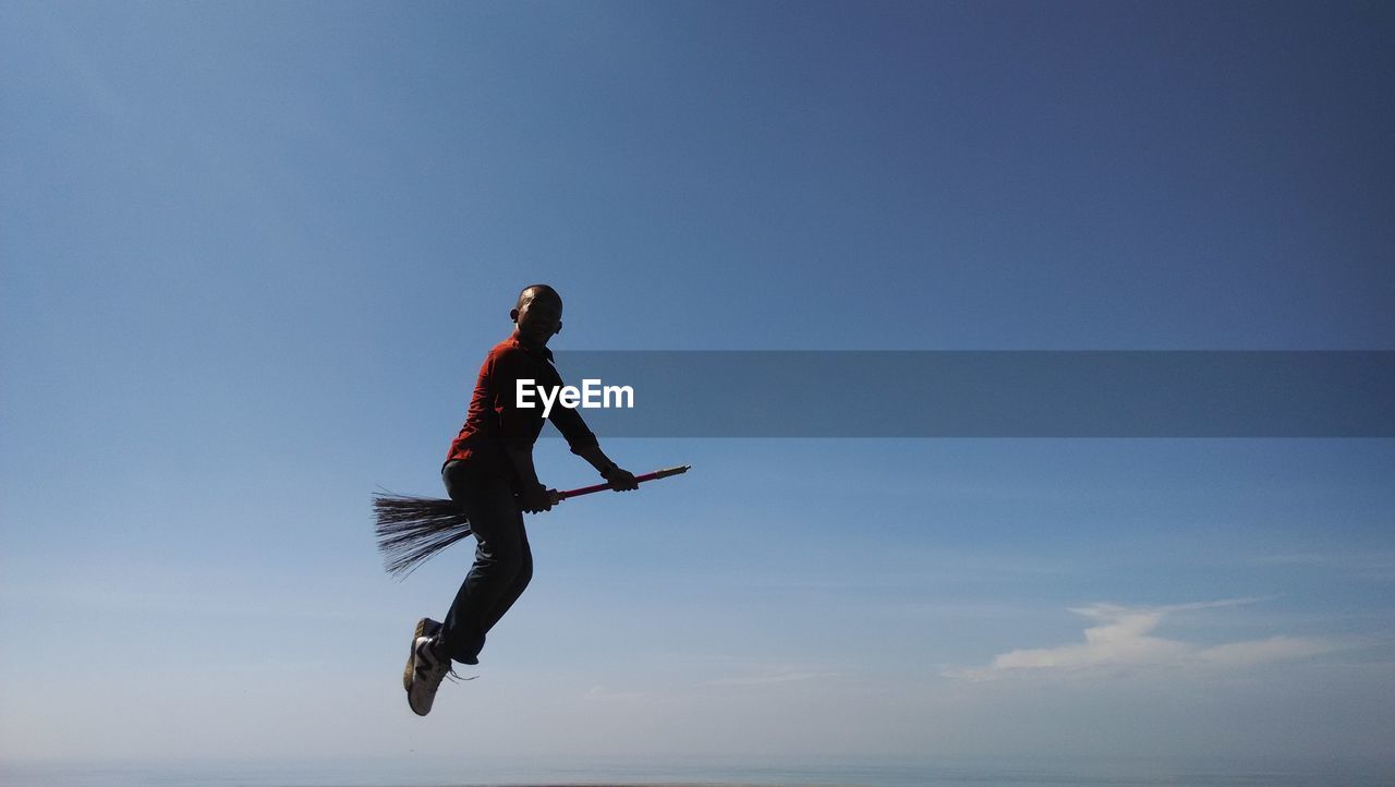 Low angle view of a man flying on broom against sky
