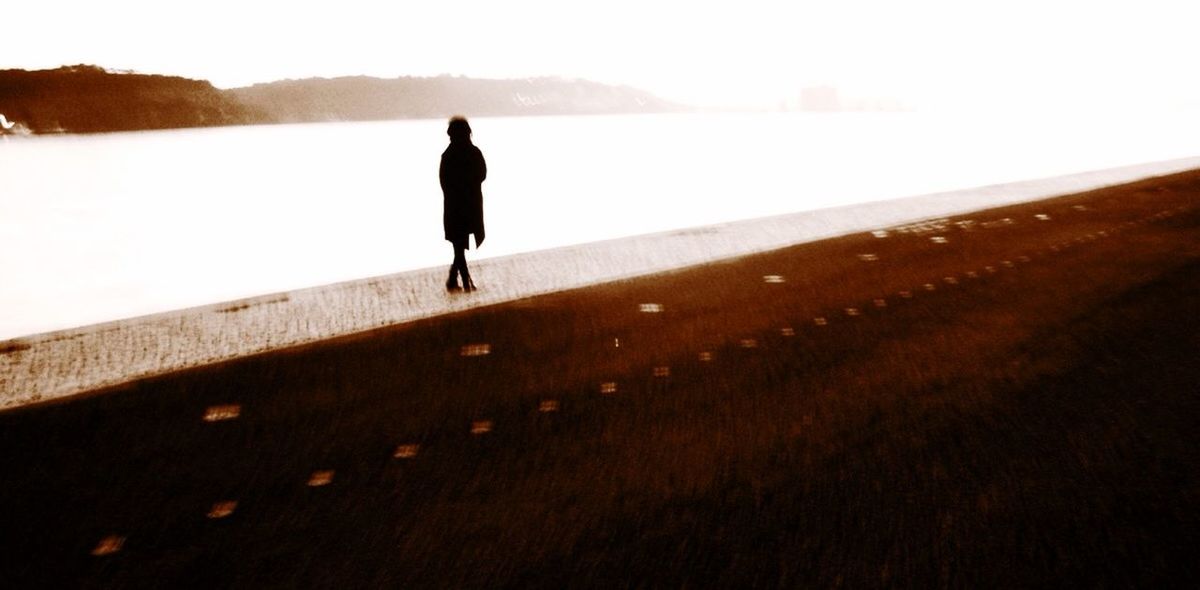 Silhouette woman walking on sidewalk amidst river and road
