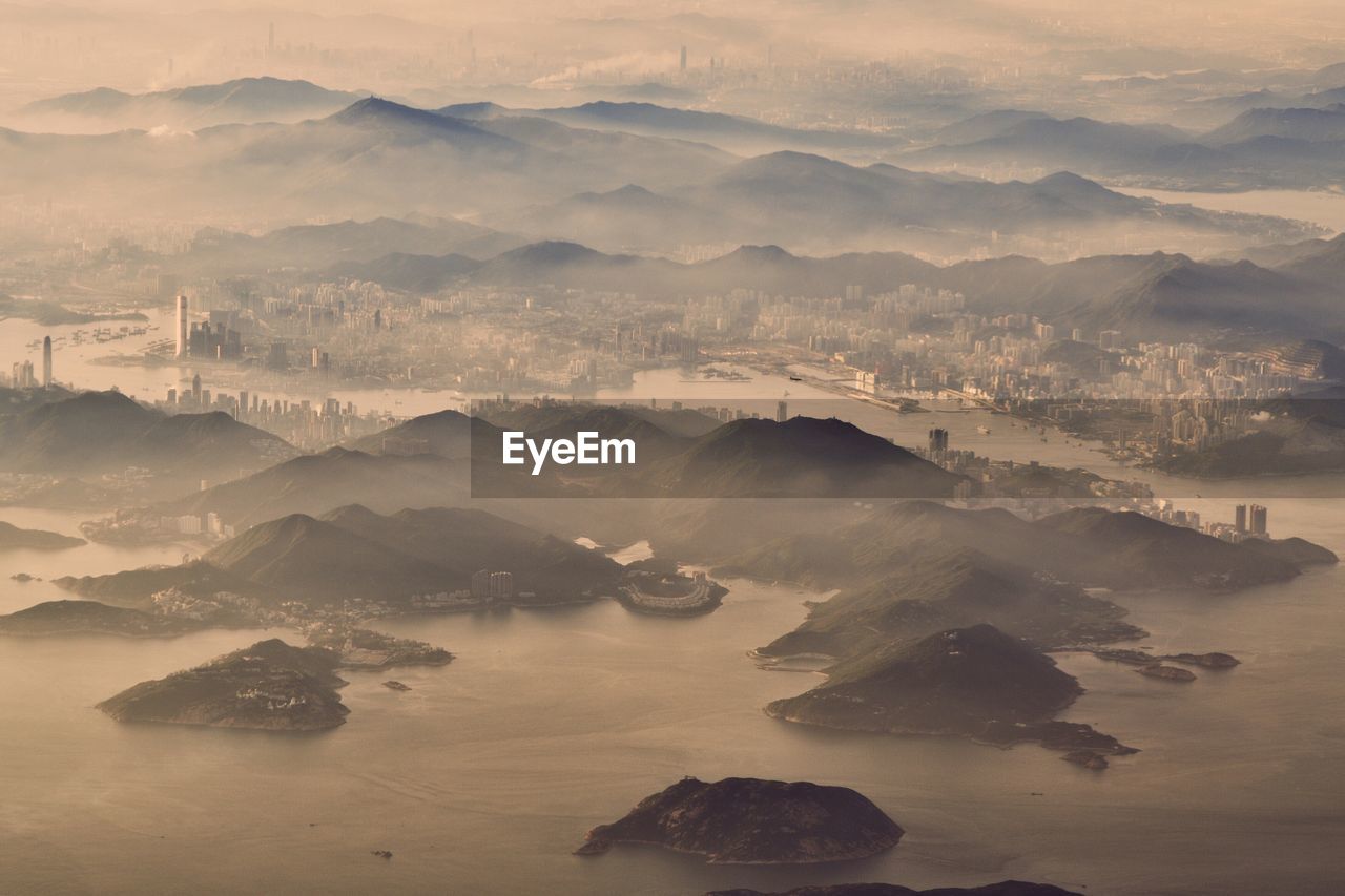 Aerial view of mountains in sea by buildings during sunset