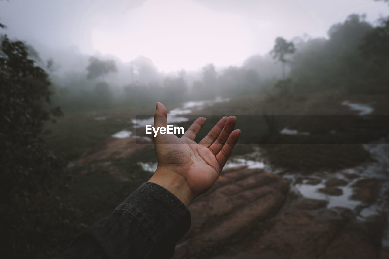 Cropped hand gesturing against sky during foggy weather